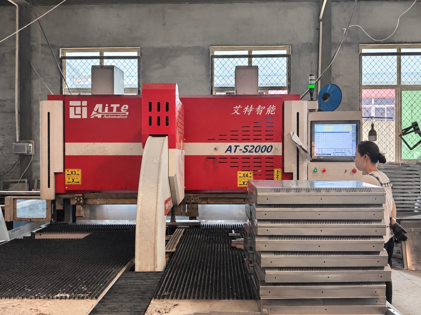 Operator at a CNC punching station beside prepared metal panels